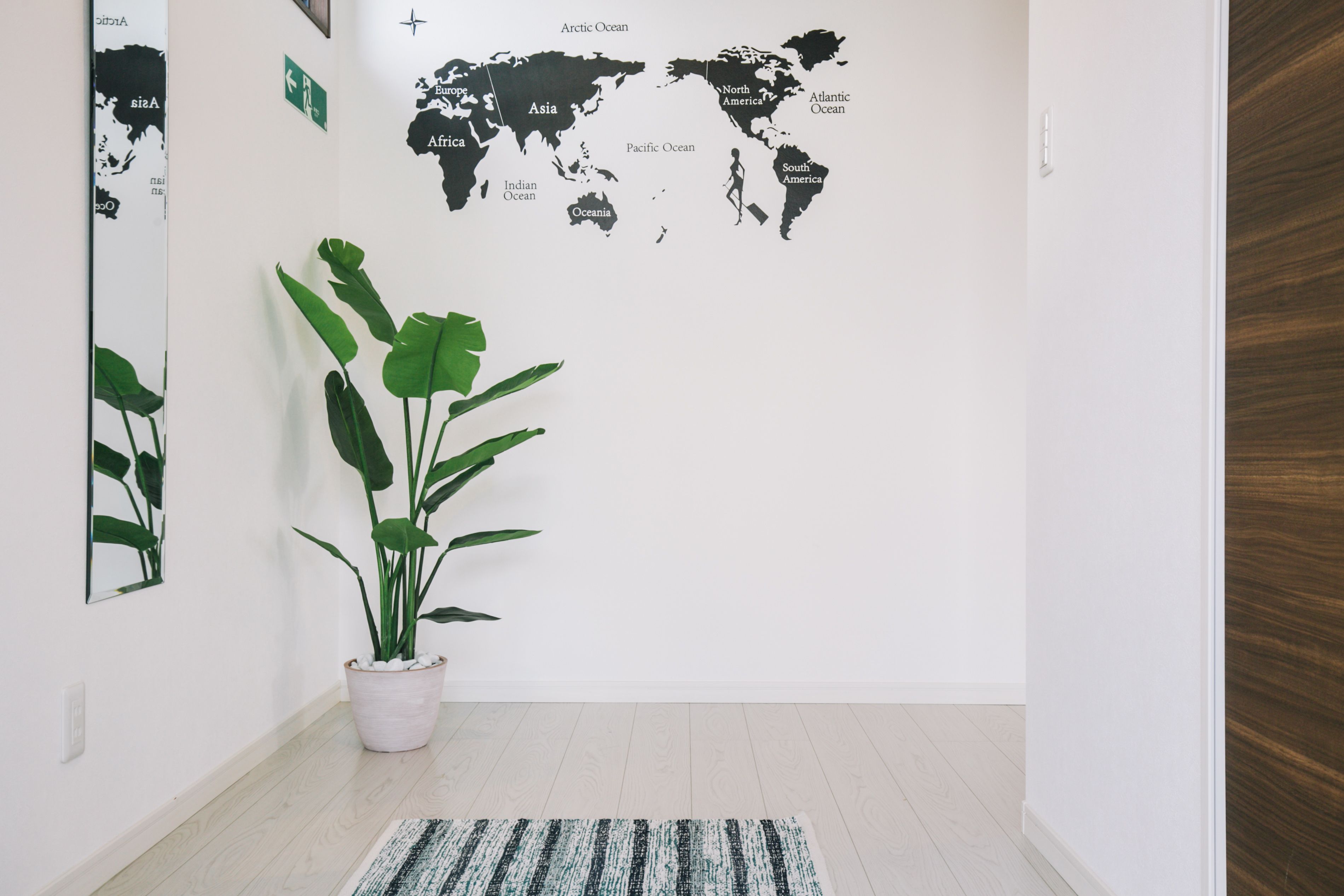 Un pasillo con un mural de un mapa mundial, una planta en maceta y un felpudo a rayas.