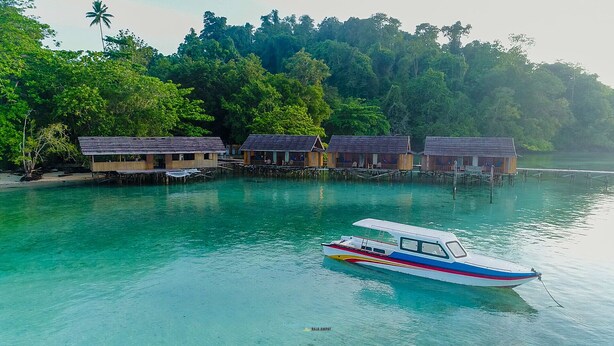 A row of wooden overwater bungalows with a boat docked in front. - HamuEco Dive Resort Raja Ampat (Waisai)
