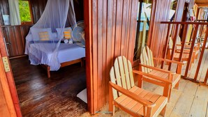 A wooden cabin with a bed under a mosquito net, wooden chairs, and a wooden floor. - HamuEco Dive Resort Raja Ampat (Waisai)