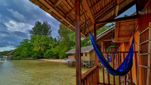 A wooden structure with a thatched roof overlooking a calm body of water, surrounded by lush greenery and palm trees. - HamuEco Dive Resort Raja Ampat (Waisai)