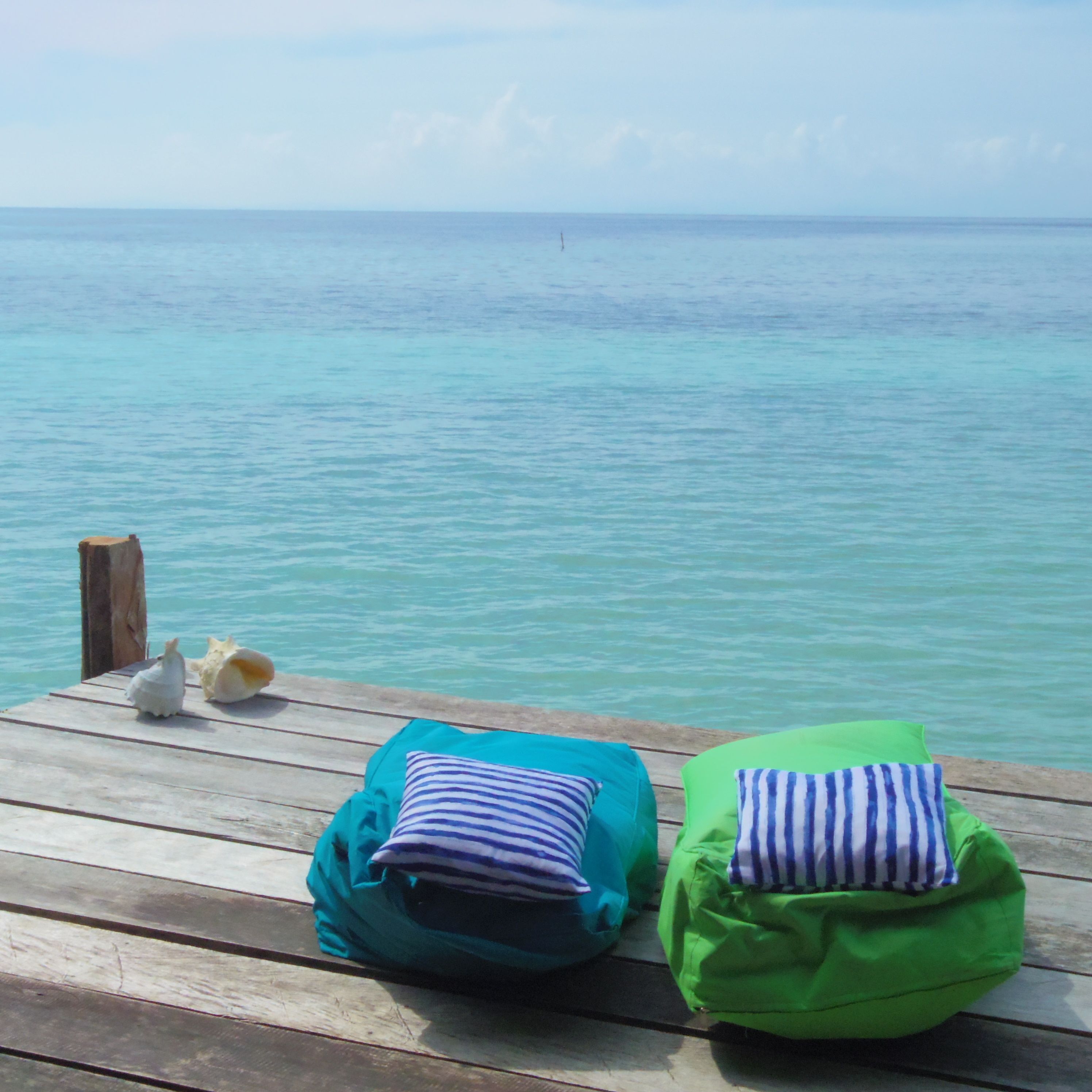 A wooden deck with two bean bags, one teal and one green, facing a calm sea.