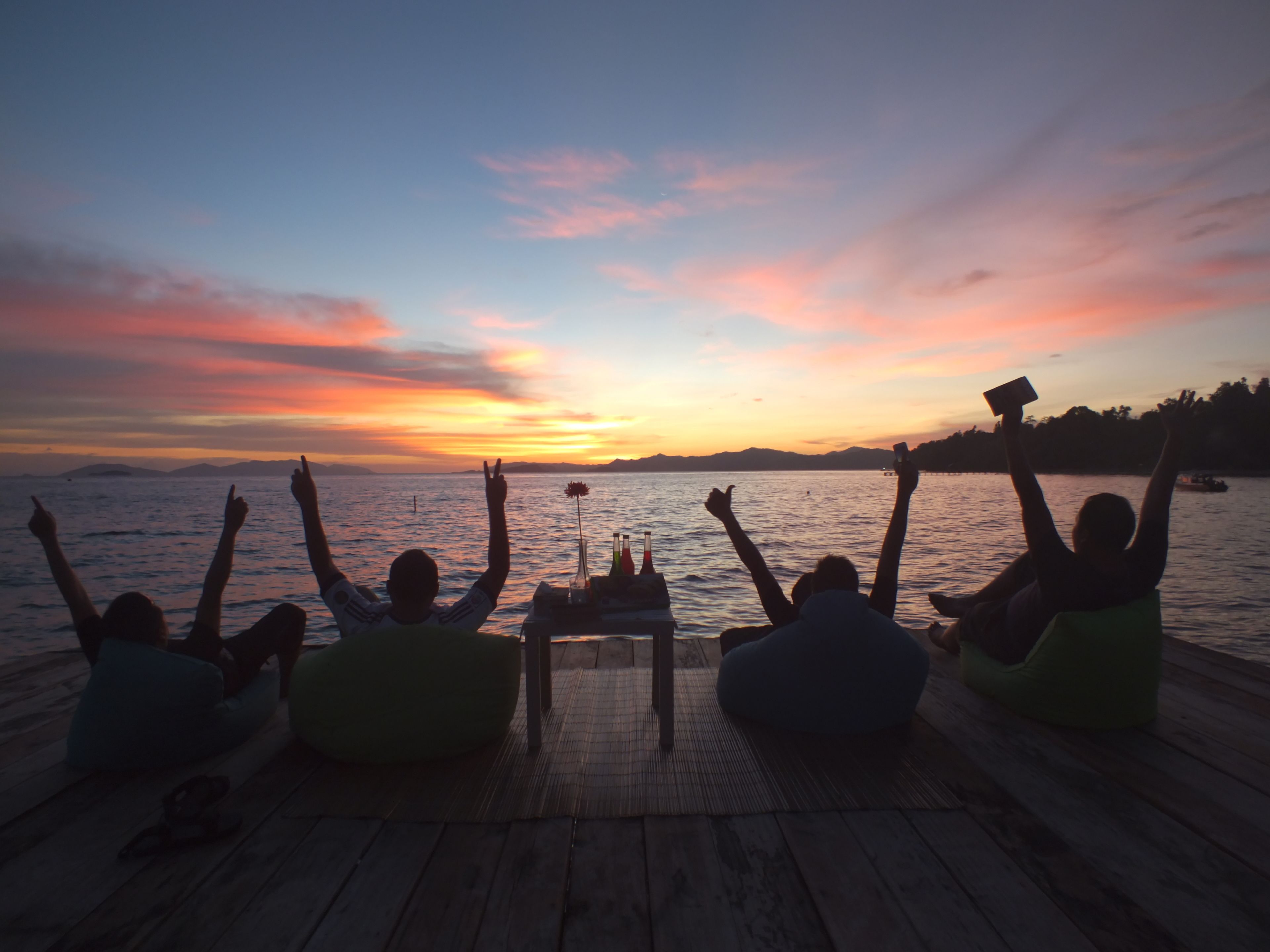 A sunset view from a wooden dock with people sitting on bean bags facing the water.