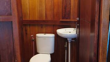 A small, wooden-paneled bathroom with a toilet and a sink.