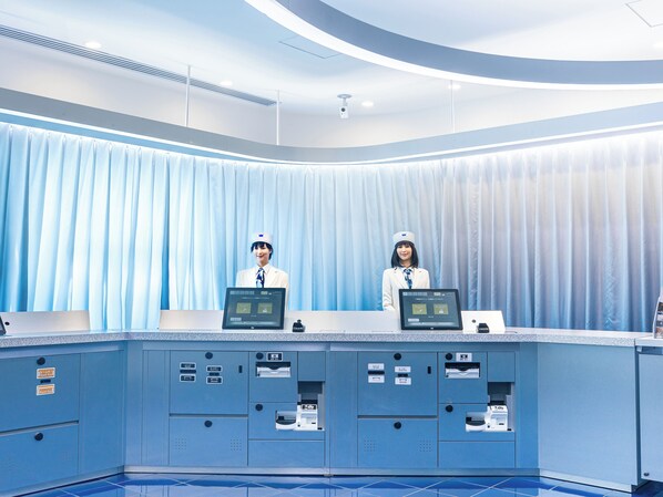 Ein Empfangsschalter mit zwei Mitarbeitern, einer blauen Wand und einem blauen Vorhang als Hintergrund.