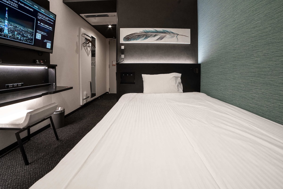 A hotel room with a bed, a desk, a TV, and a wall-mounted artwork.