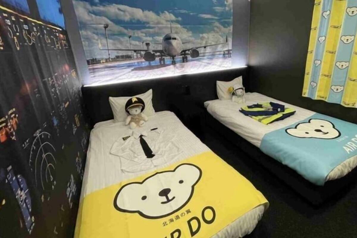 Two beds with bear-themed bedding, a poster of an airplane on the wall, and a window with a view of the sky.
