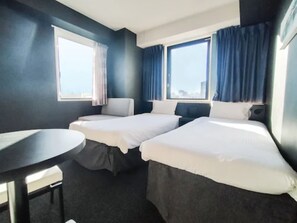 Ein Hotelzimmer mit zwei Betten, einem kleinen runden Tisch und großen Fenstern mit Vorhängen.