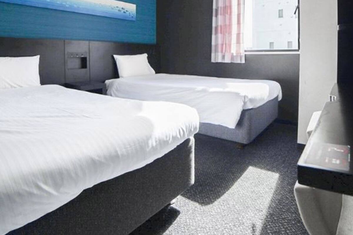 A hotel room with two beds, a small desk, and a window with curtains.
