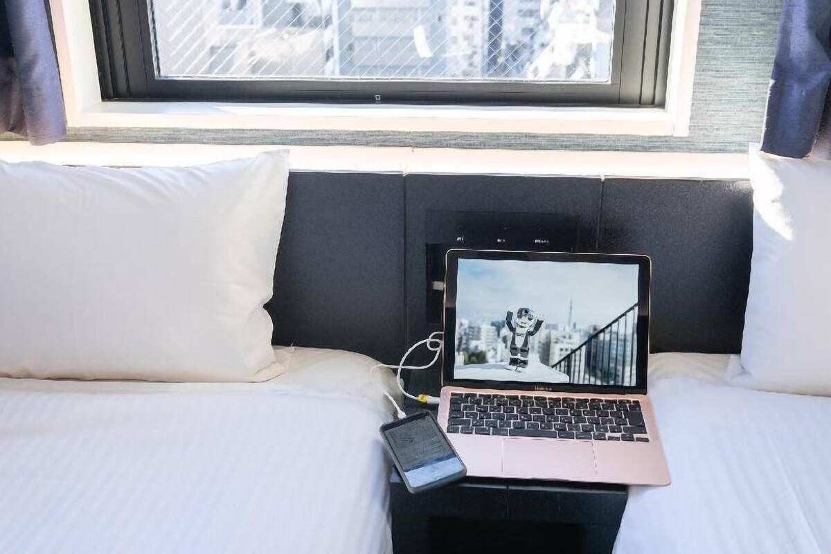 Ein Bett mit Laptop und Smartphone, ein Fenster mit Blick auf die Stadt und ein schwarzes Kopfteil.
