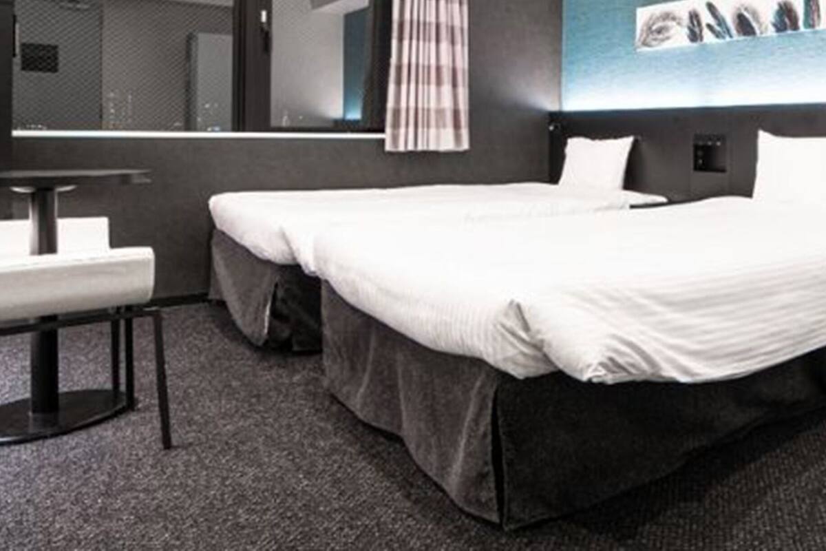 A hotel room with two beds, a sofa, a small table, and a large window with a view of the sea.