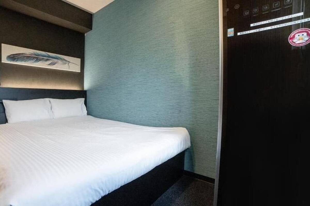 Ein Hotelzimmer mit einem Bett, einem Wandbild, einer Tür und einer Bedienkonsole.