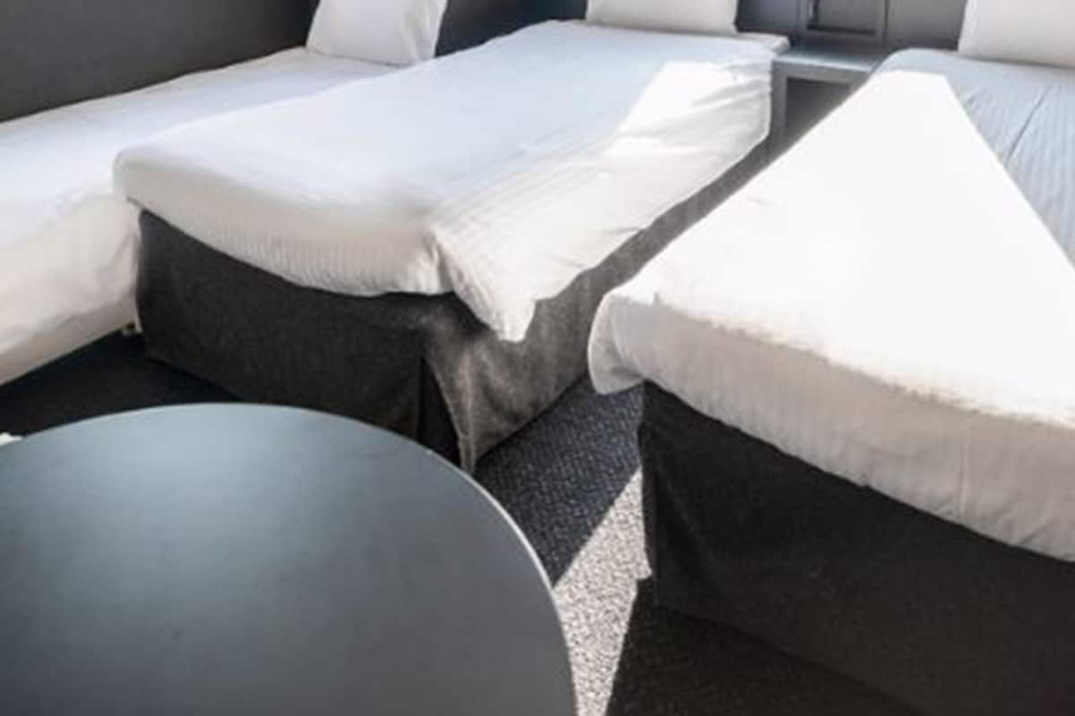 A room with three beds arranged in a row, each with white bedding.