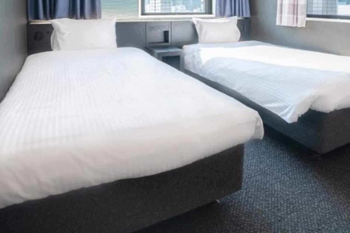 A hotel room with two single beds, a small bedside table, a nightstand, and a window with curtains.
