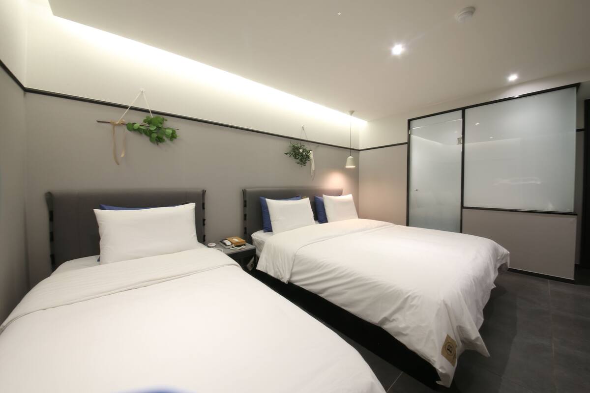 A modern hotel room with two beds, a bedside table with a lamp, and a large sliding door closet.