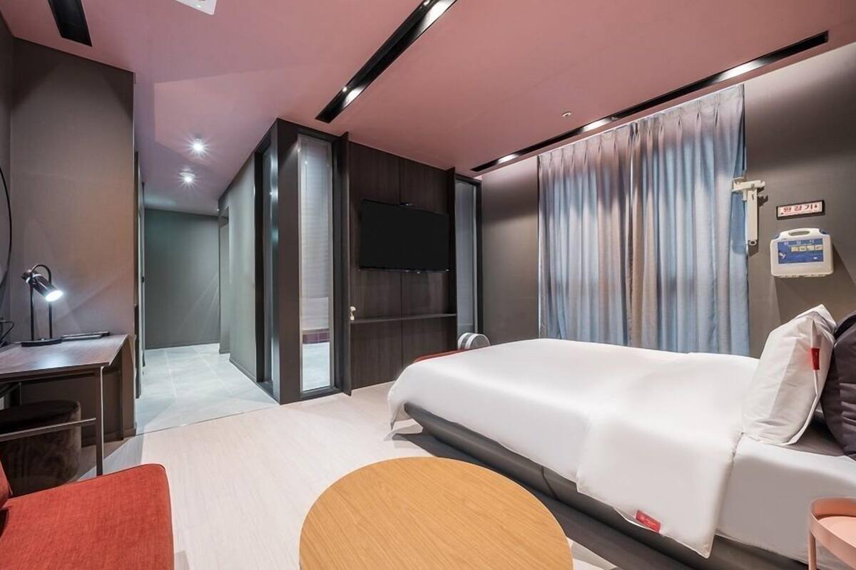 A modern hotel room with a large bed, a desk with a mirror, a TV, and a bedside table.