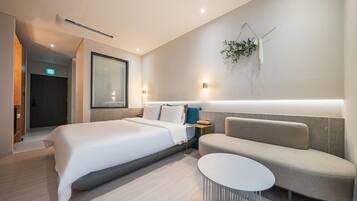 Ein modernes Hotelzimmer mit einem großen Bett, einem Nachttisch, einem kleinen runden Tisch und einer Wandleuchte.