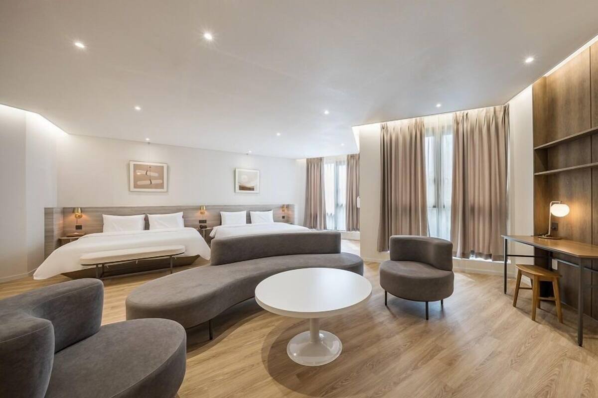 A modern hotel room with a large bed, two sofas, a round table, and a desk.