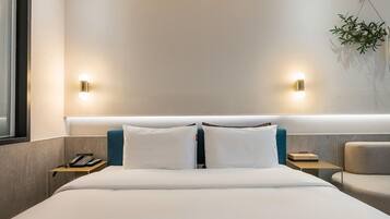 Habitación de hotel con una cama grande, dos mesitas de noche, una lámpara de noche y una planta en la pared.