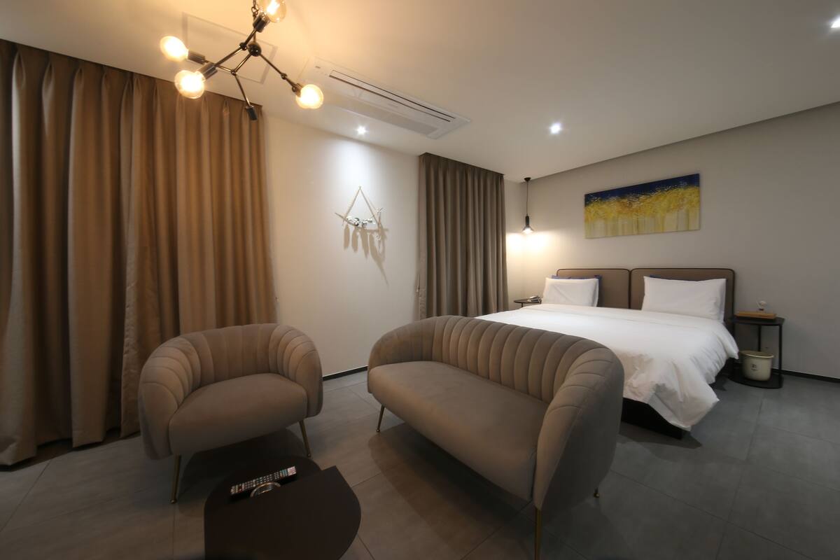 A modern hotel room with a bed, two sofas, a small table, and a painting on the wall.