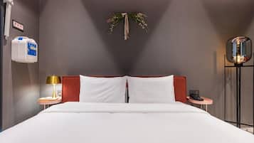 A hotel room with a bed, a bedside table with a lamp, a bedside phone, and a wall-mounted air purifier.