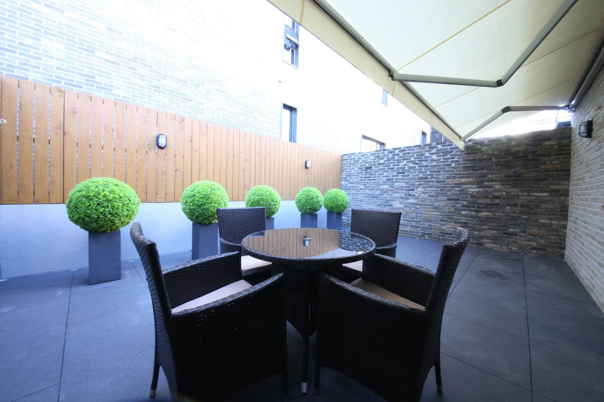 A patio area with a round table and six chairs, surrounded by potted spherical plants.