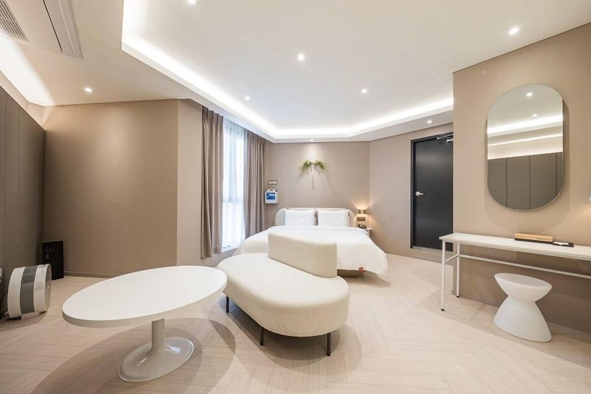 A modern hotel room with a bed, bedside table, lamp, and a round mirror.