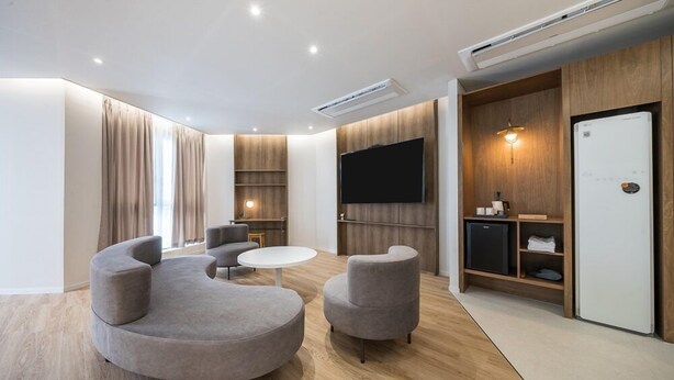 A modern living room with a curved sofa, two armchairs, a round coffee table, a flat-screen TV, and built-in shelving. - Brown Dot Hotel Masan (Changwon)