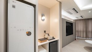 A modern hotel room with a built-in LG refrigerator, a flat-screen TV mounted on the wall, a small coffee table with a book and mugs, and a compact black refrigerator. - Brown Dot Hotel Masan (Changwon)
