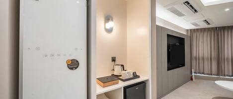 A modern hotel room with a built-in LG refrigerator, a flat-screen TV mounted on the wall, a small coffee table with a book and mugs, and a compact black refrigerator.