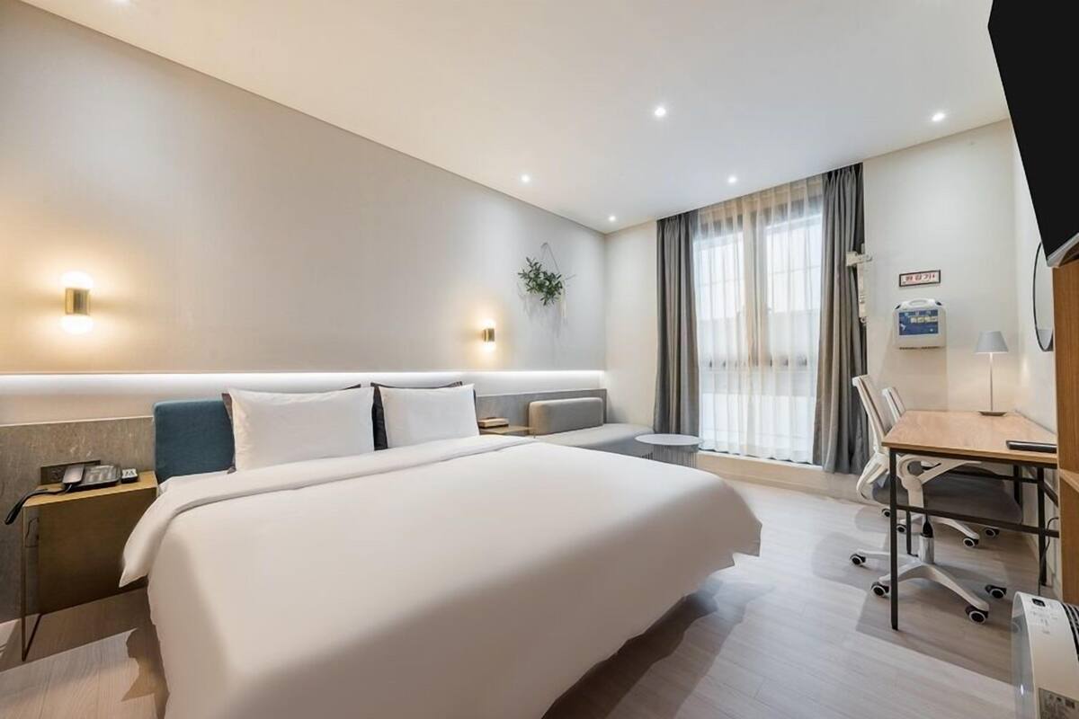 A modern hotel room with a large bed, a desk, and a chair.