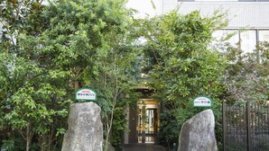 A hotel entrance with a pathway flanked by large rocks and lush greenery, leading to a glass door entrance. - Hotel Hakata Nakasu Inn (Fukuoka)