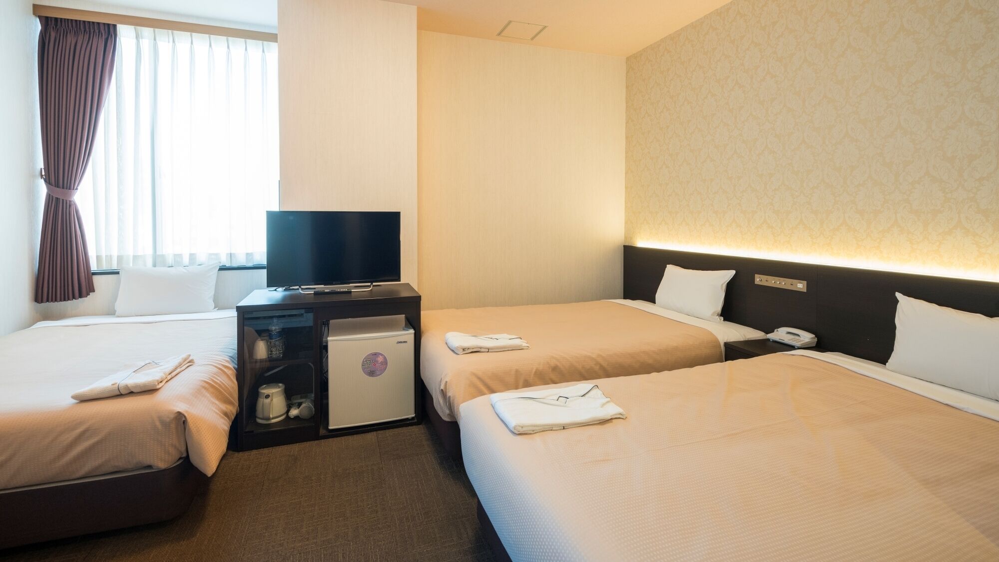 Habitació d'hotel amb dos llits, una taula de nit amb televisió, minibar i un telèfon fixat a la paret.