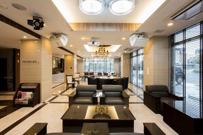 Een moderne hotellobby met een receptiebalie, een zithoek en een stadszicht door grote ramen.