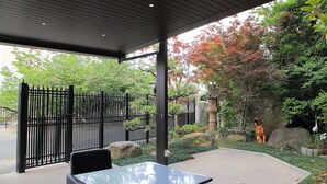 An outdoor seating area with a table and chairs, a black metal fence, and a stone lantern. - Hotel Hakata Nakasu Inn (Fukuoka)