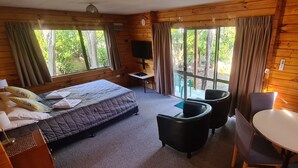 A wooden cabin room with a bed, a desk, a chair, and a table. - Forest Peak Motel (Hanmer Springs)