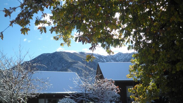 A cabin with a snow-covered roof, surrounded by trees and mountains in the background. - Forest Peak Motel (Hanmer Springs)