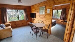 A cozy room with wooden walls, a sofa, a dining table with chairs, and a TV mounted on the wall. - Forest Peak Motel (Hanmer Springs)