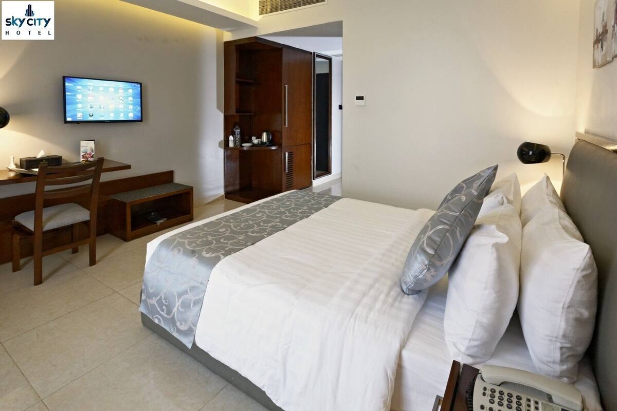 Habitación de hotel con cama, mesita de noche y escritorio con silla. Hay un televisor en la pared y un armario al fondo.