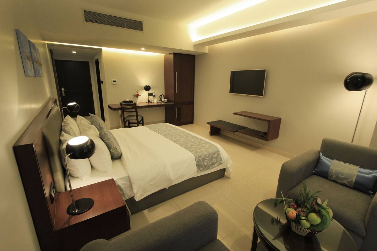 Una habitación de hotel moderna con cama, sofá, televisión, escritorio y una mesita con una cesta de frutas.