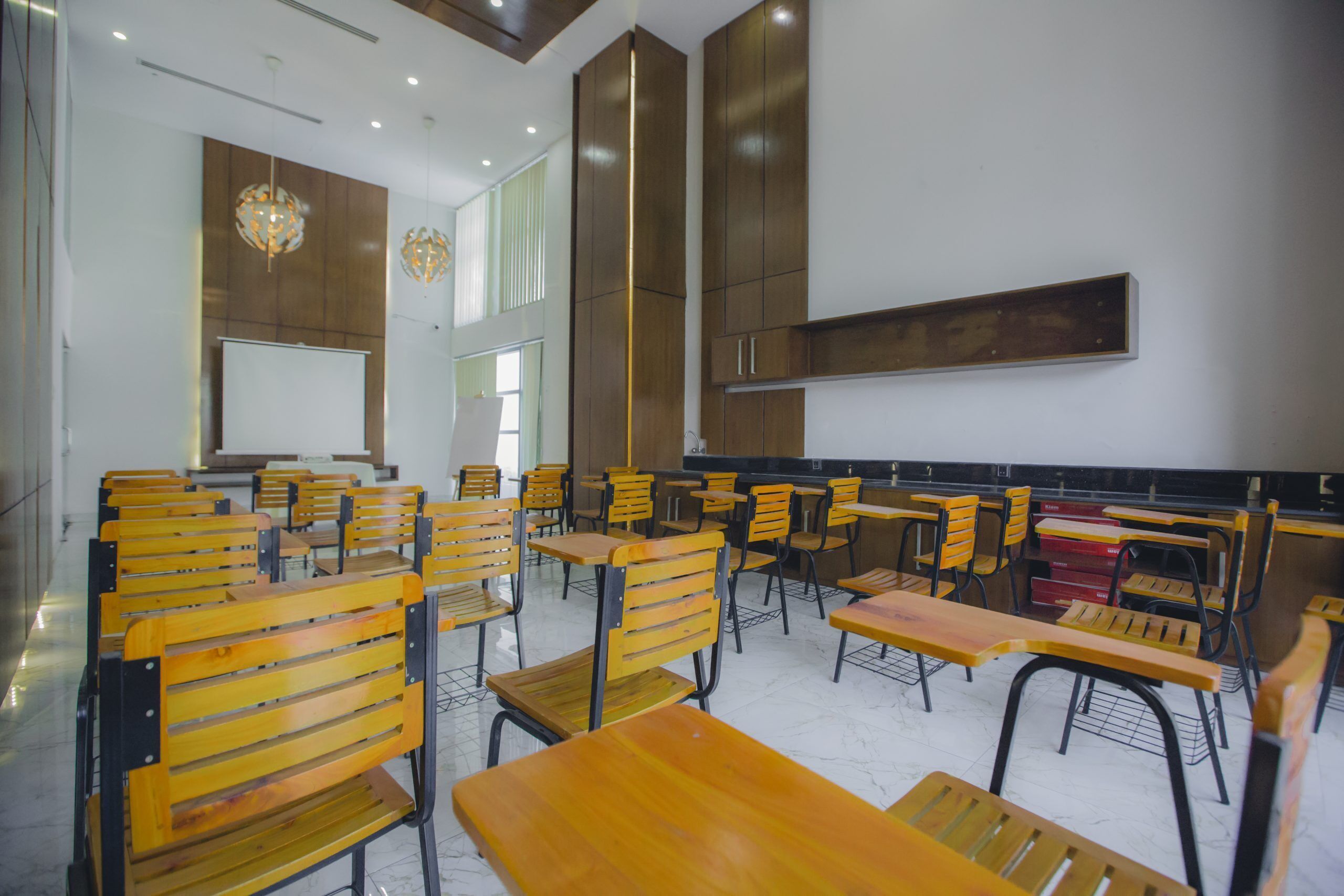 A classroom with wooden desks and chairs, a whiteboard, and a large cabinet.