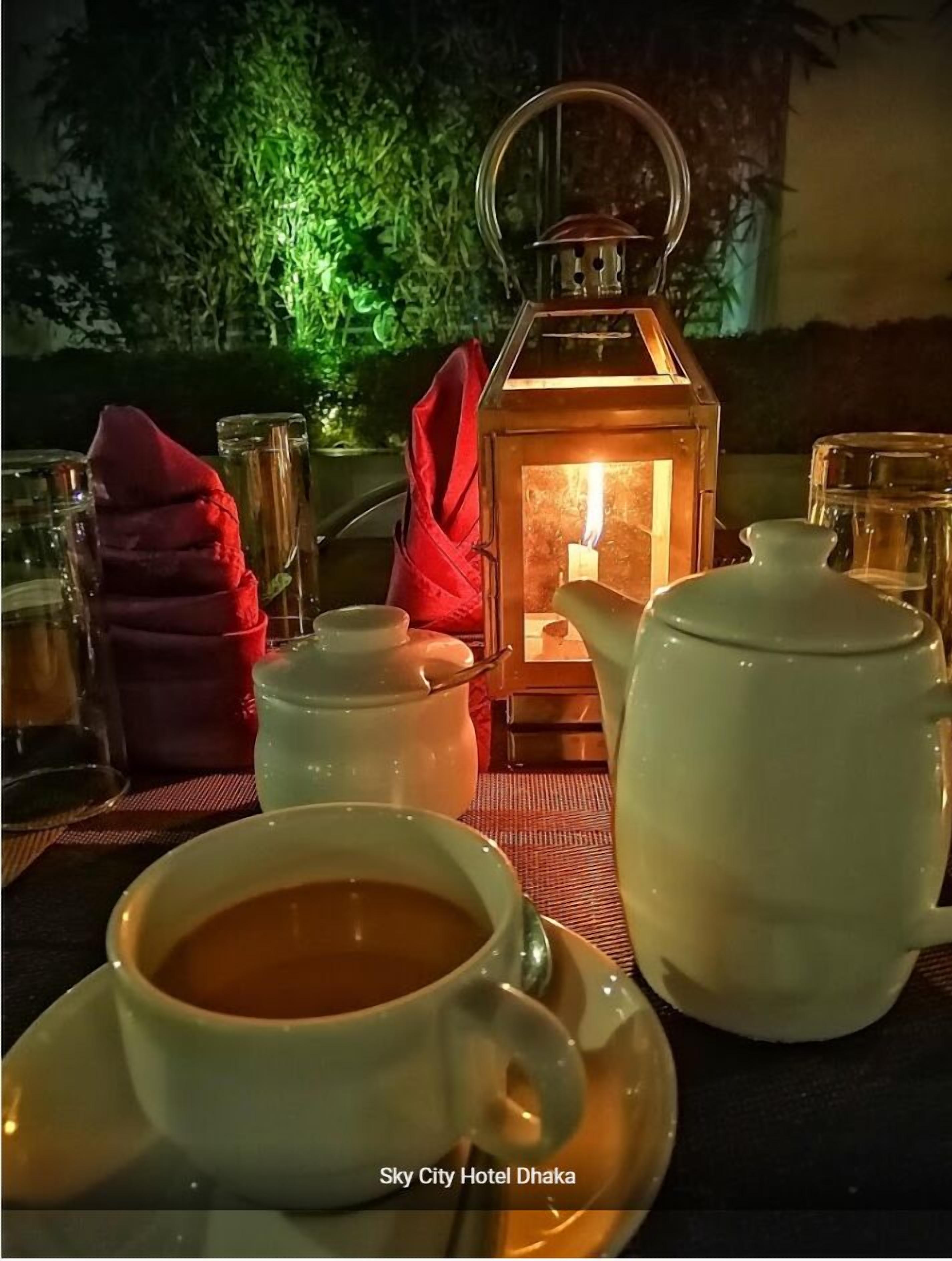 A table set with a teapot, cups, and a lantern in a dimly lit outdoor setting.