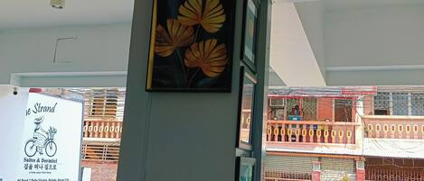 A hotel interior with a framed floral artwork on a pillar, a signboard with hotel details, and a view of the street outside.