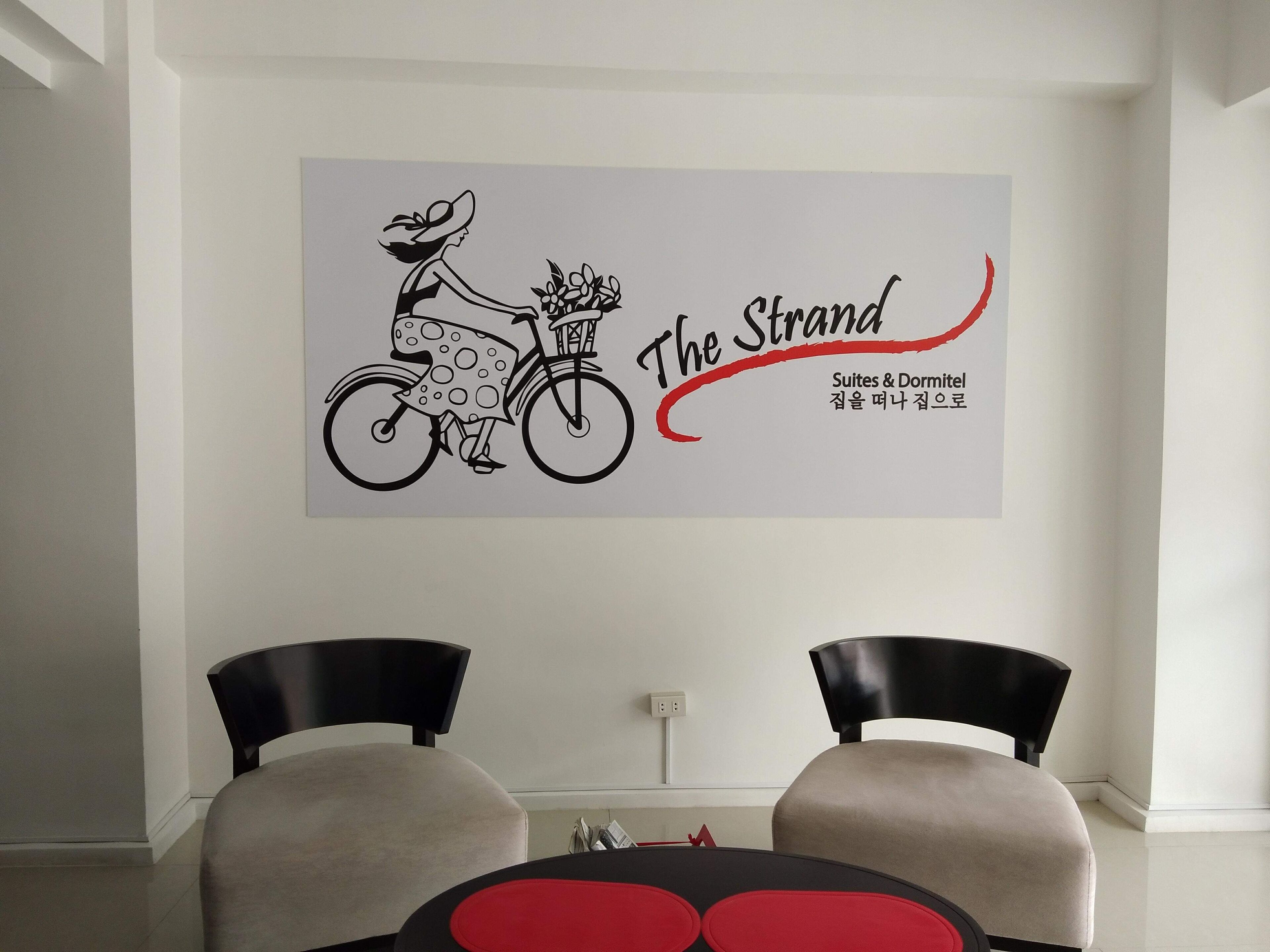 Uma parede com um desenho de uma mulher de bicicleta e o texto "The Strand Suites & Dormitory".