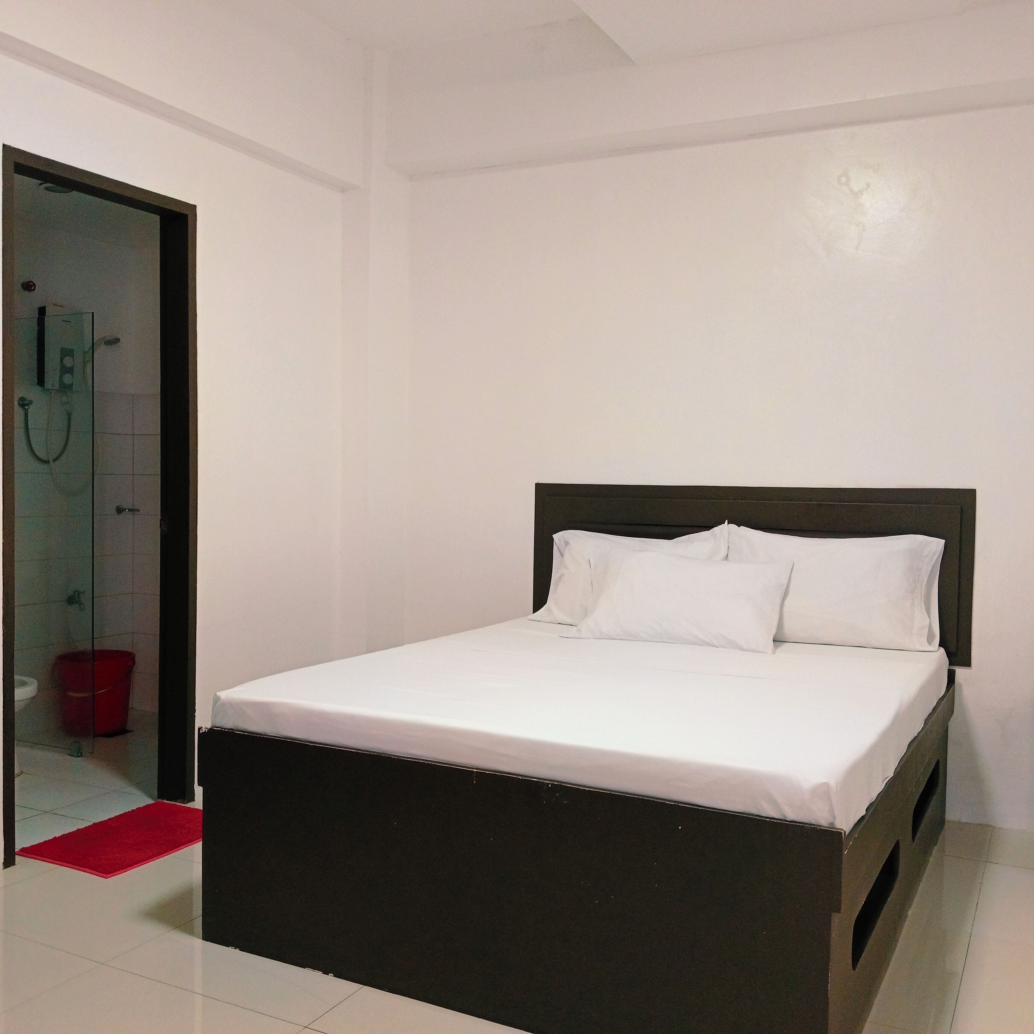 A single bed with white bedding in a room with white walls and a dark headboard.