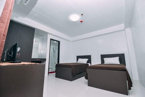 Una habitación de hotel con dos camas individuales, un escritorio con una computadora y un espejo.