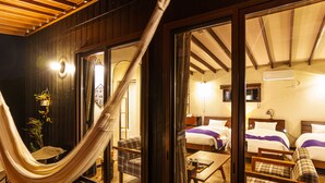 A room with a hammock, two beds, a table, and a chair.