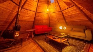 A cozy, wooden-roofed interior with a red sofa, a glass coffee table, and a small rug.