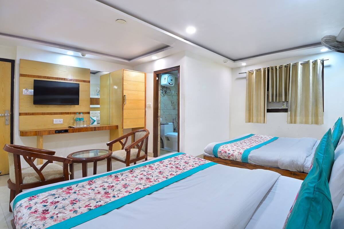 A hotel room with two beds, a desk, a chair, a television, and a bathroom visible through an open door.