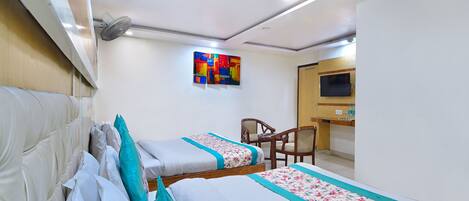 A hotel room with two beds, a desk, a chair, a TV, and a ceiling fan.