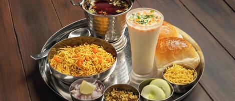 A meal tray with various Indian dishes including noodles, a milkshake, and a bread roll.